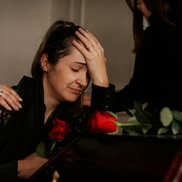 Trauernde Frau stützt sich auf einen Sarg, Hände auf ihren Schultern