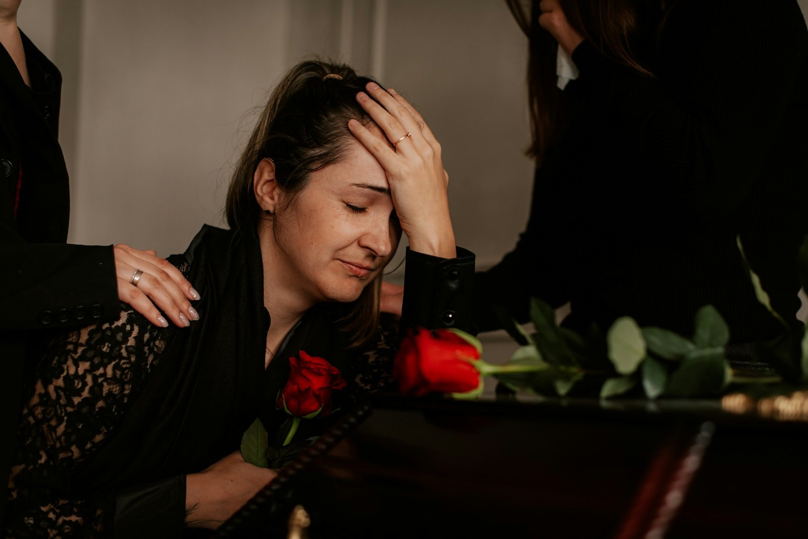 Trauernde Frau stützt sich auf einen Sarg, Hände auf ihren Schultern