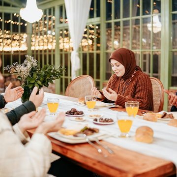 Vier Personen sitzen an einem Tisch. Sie halten die Hände zum Gebet nach oben. Zwei Frauen tragen ein Kopftuch