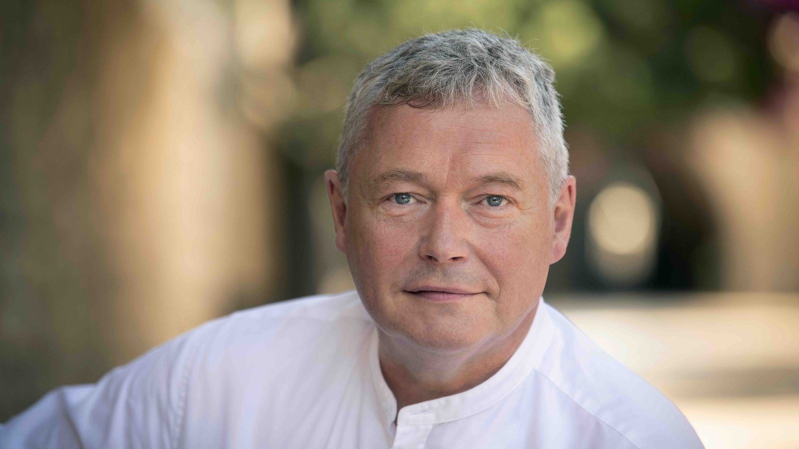 Portraitfoto von Joachim Lenz, der evangelischer Probst in Jerusalem ist. Der Mann hat graue Haare, trägt ein weißes Hemd und schaut in die Kamera.