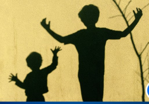 eine gelbe Mauer auf der der Schatten eines größeren und kleineren Kindes zu sehen sind, die beide ihre Arme nach oben heben.