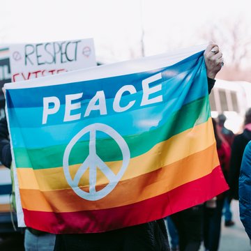 Demonstrierende mit Regenbogenflagge auf der PEACE (Frieden) steht.