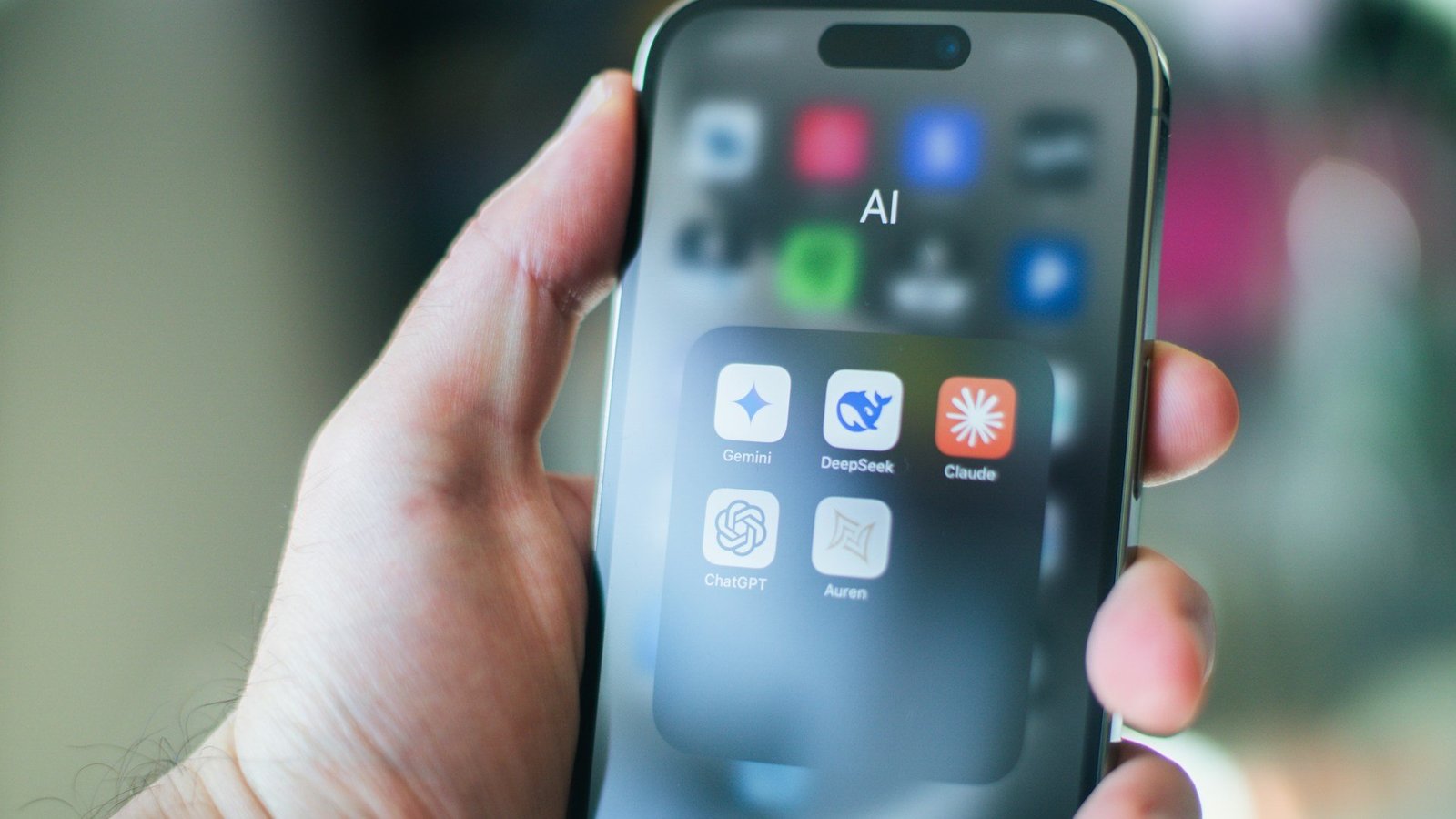 Eine Hand hält ein Handy auf dessen Bildschirm verschiedene KI (Künstliche Intelligenz)-Apps zu sehen sind.