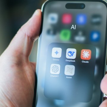 Eine Hand hält ein Handy auf dessen Bildschirm verschiedene KI (Künstliche Intelligenz)-Apps zu sehen sind.