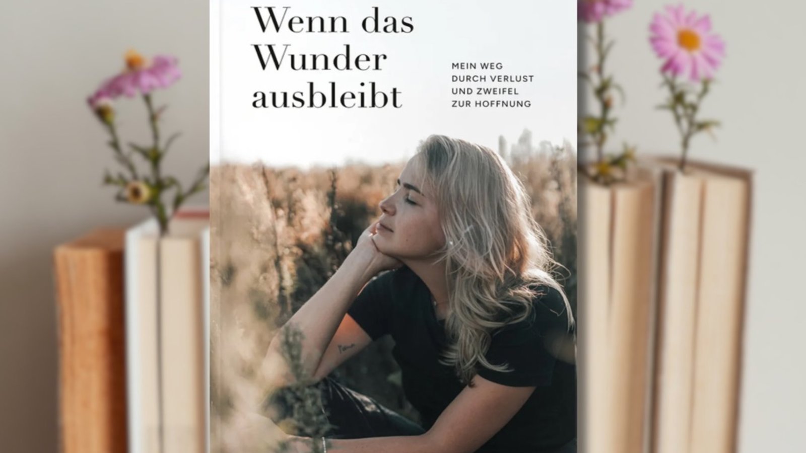 Buchcover "Gianna Wemmer: Wenn das Wunder ausbleibt" im Vordergrund, Bücher, in die rosa Blumen gesteckt sind, im Hintergrund