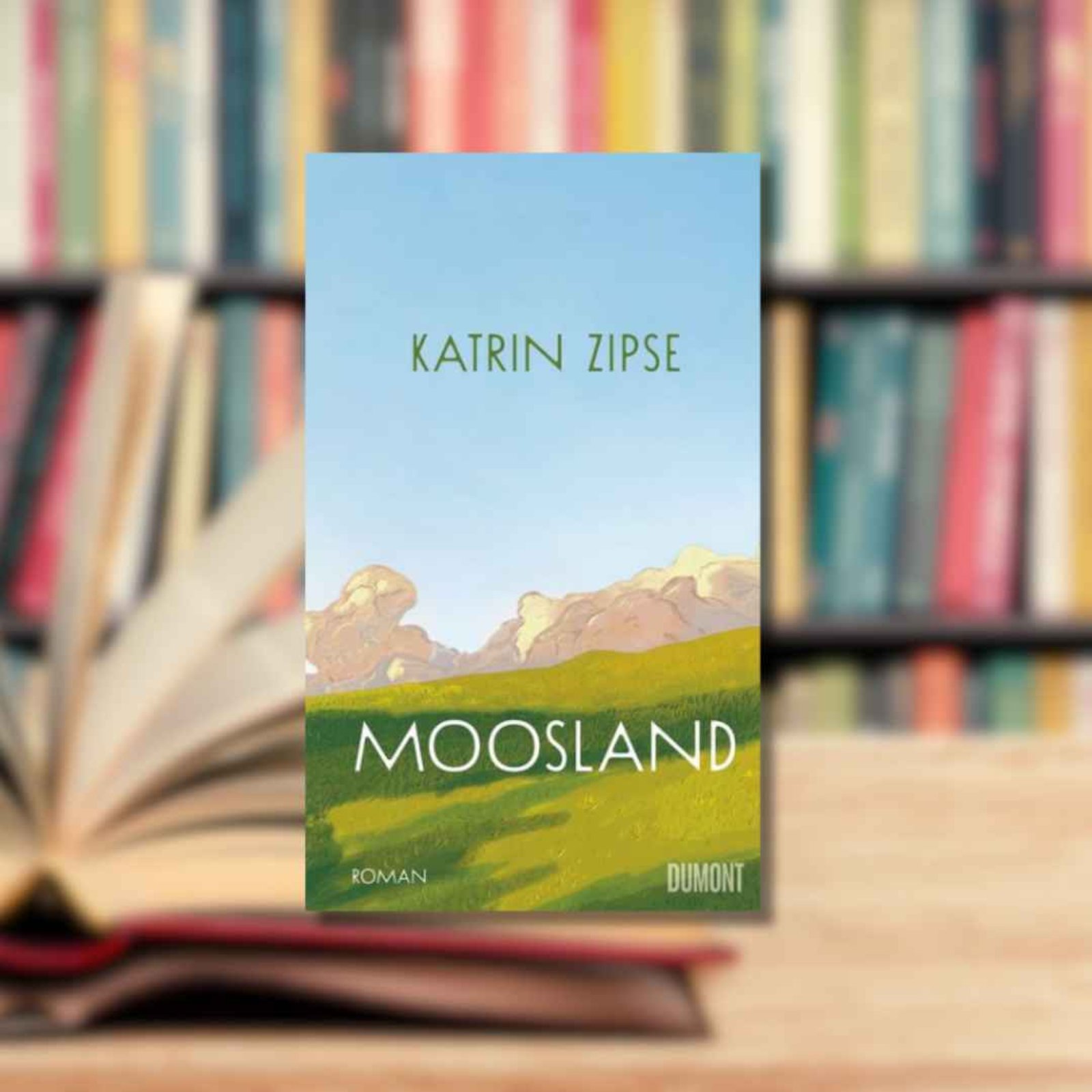 Buchtipp: „Moosland“ im Vordergrund. Im Hintergrund ist ein aufgeschlagenes Buch zu sehen.