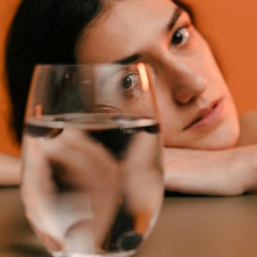 Frau legt Kopf auf einen Tisch und blickt auf ein gefülltes Wasserglas