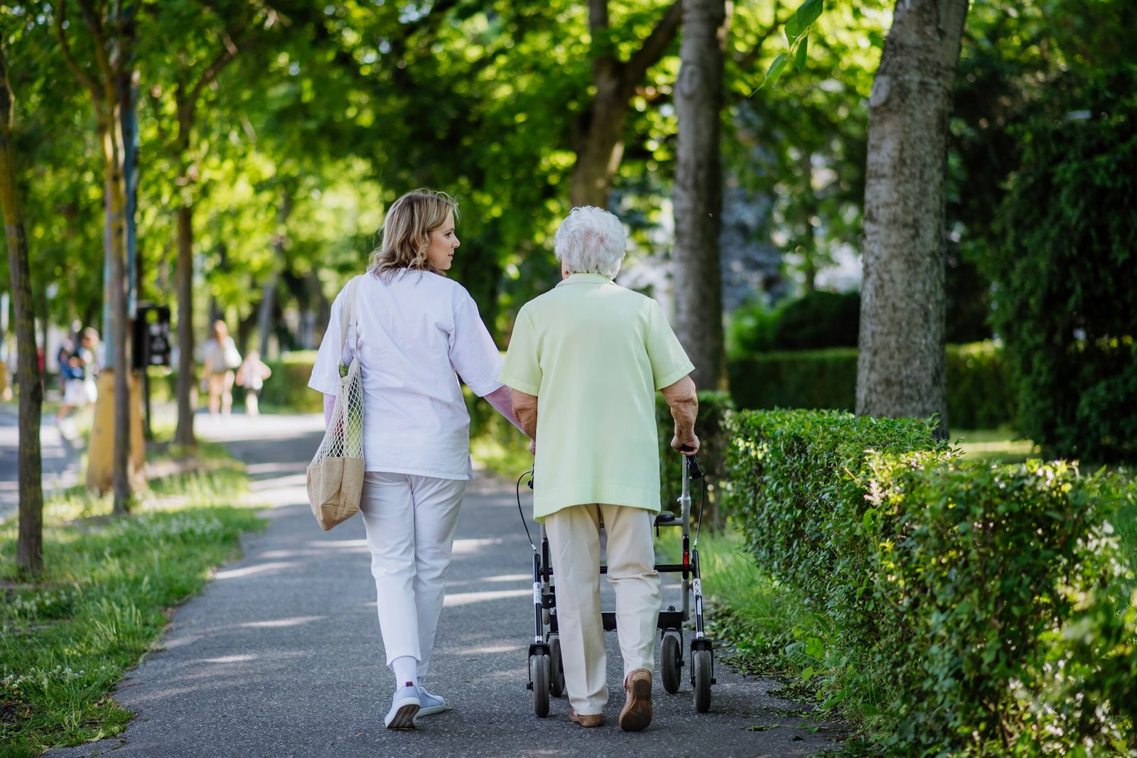 Pflegekraft geht mit Seniorin spazieren.