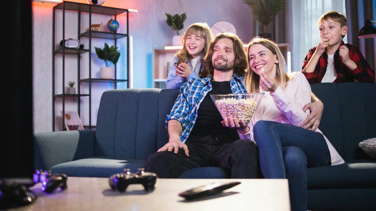 Familie mit zwei Kindern sitzt auf einem Sofa und schaut fern.
