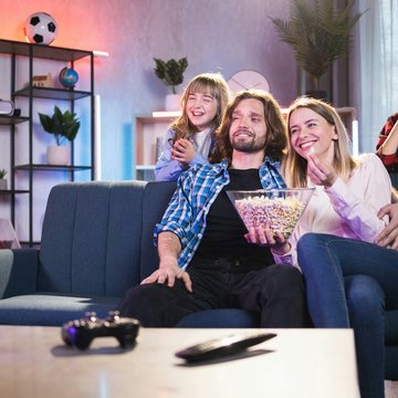 Familie mit zwei Kindern sitzt auf einem Sofa und schaut fern.