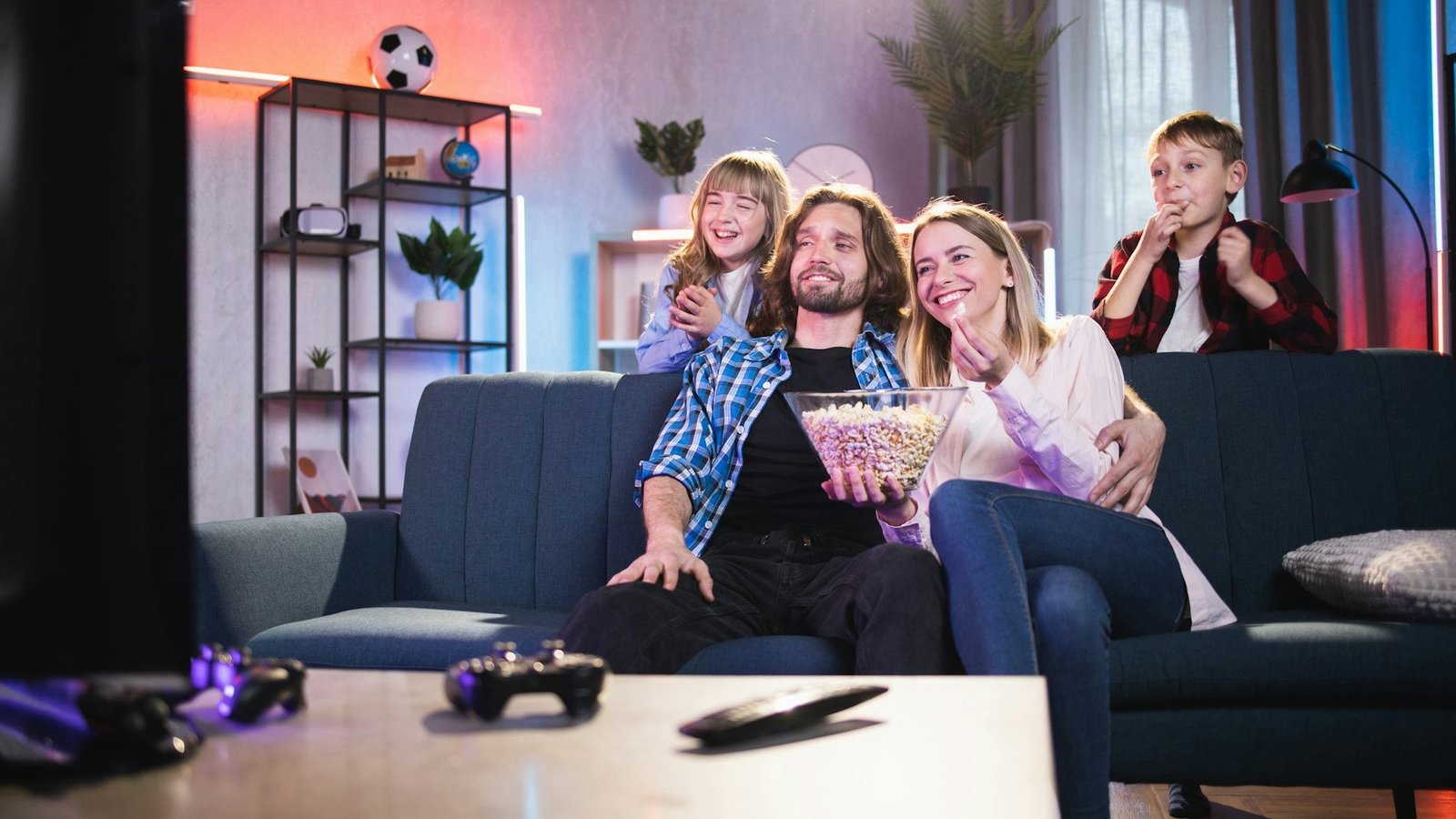 Familie mit zwei Kindern sitzt auf einem Sofa und schaut fern.