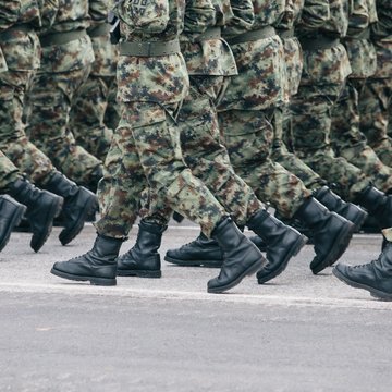 Personen in grün-braunen Uniformen (Tarnuniform) laufen synchron nebeneinander.