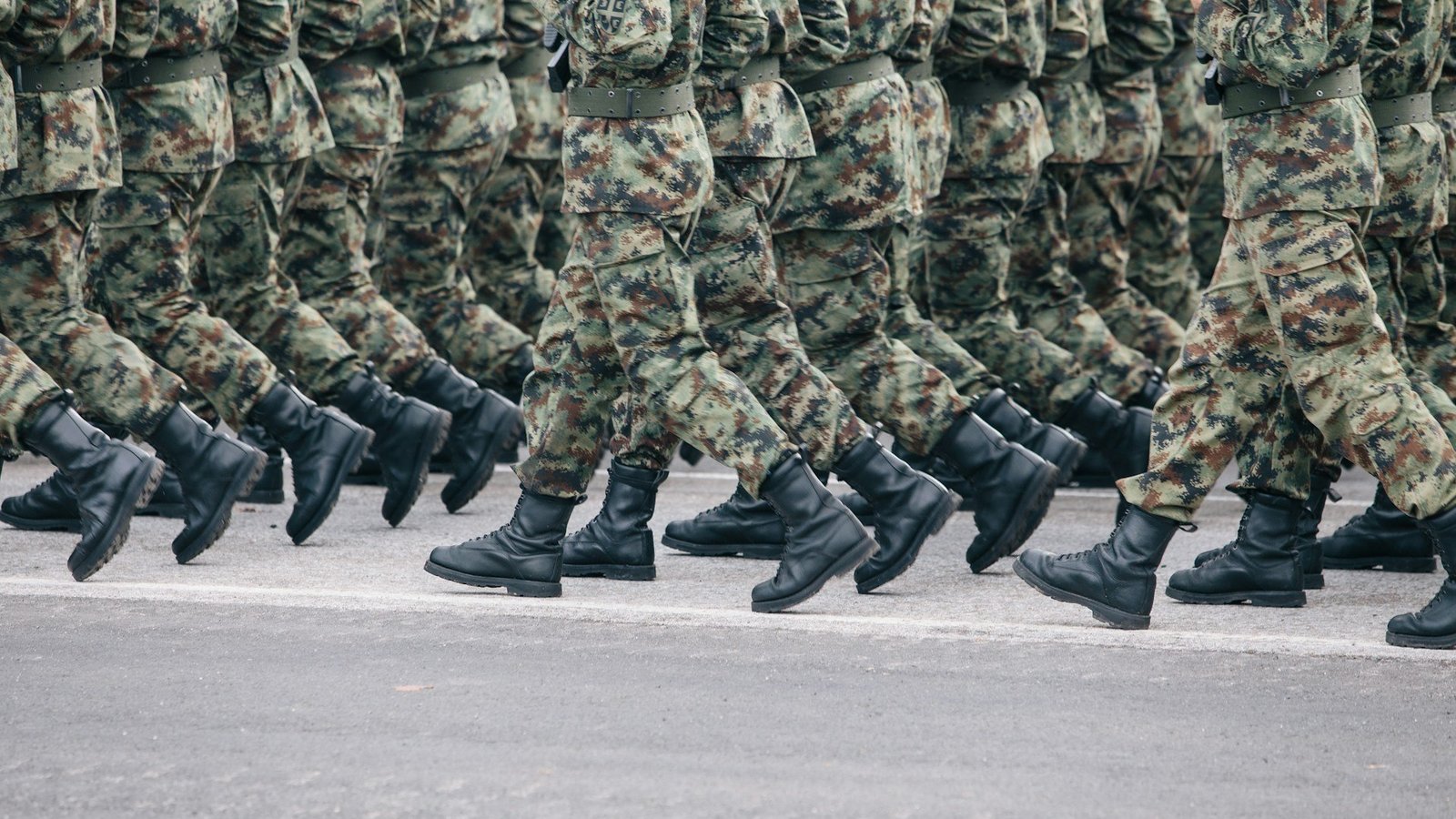 Personen in grün-braunen Uniformen (Tarnuniform) laufen synchron nebeneinander.
