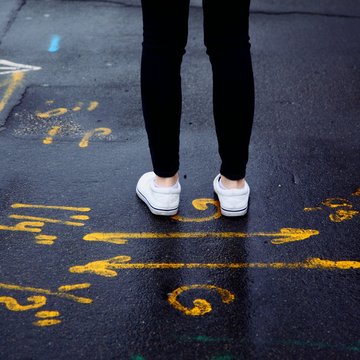 Person steht hinter zwei auf den Boden gemalten Pfeilen, die in gegenseitige Richtungen zeigen.