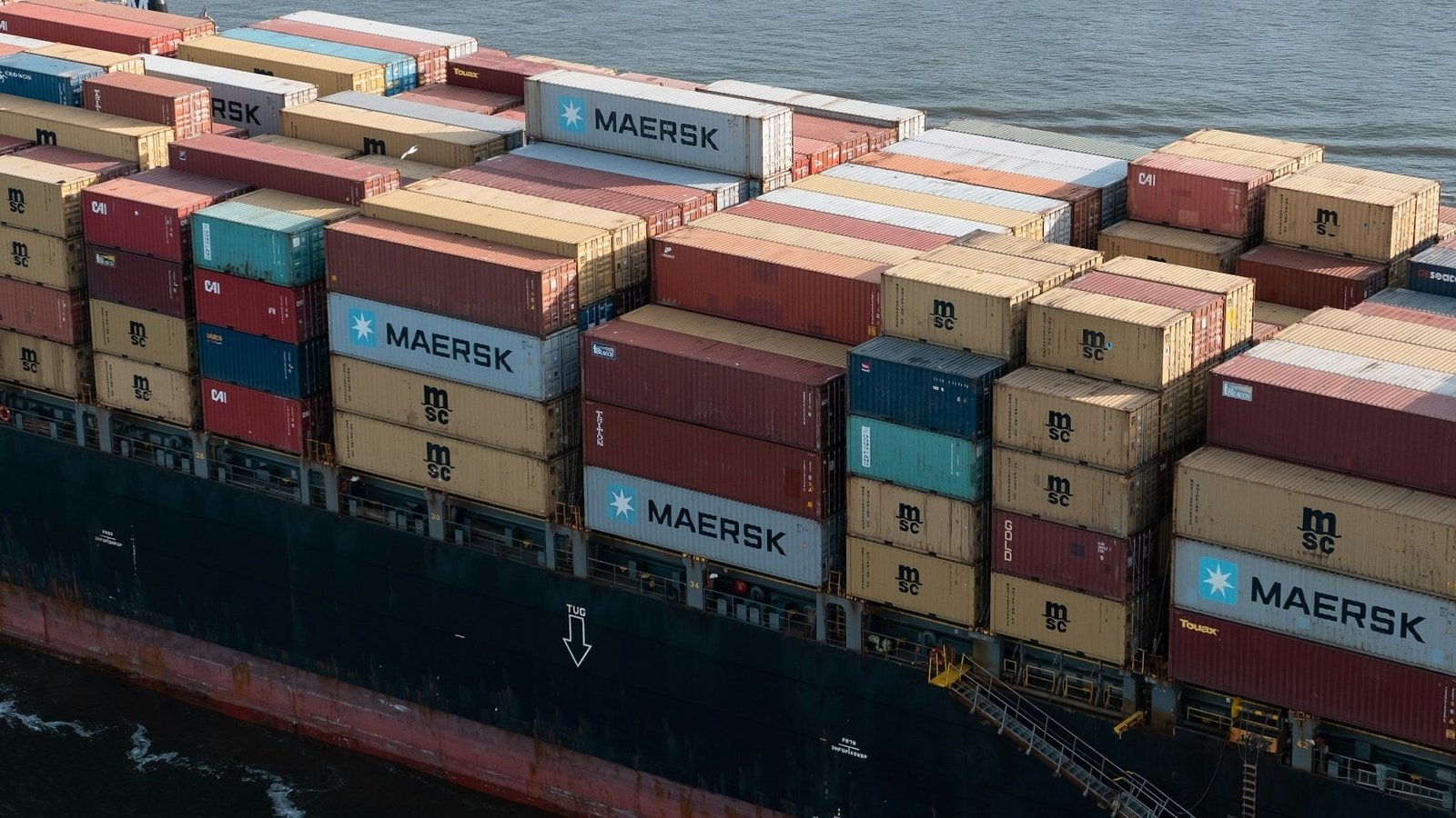 Auf dem Bild ist ein Ausschnitt eines Containerschiffes zu sehen, das mit bunten Containern beladen ist.