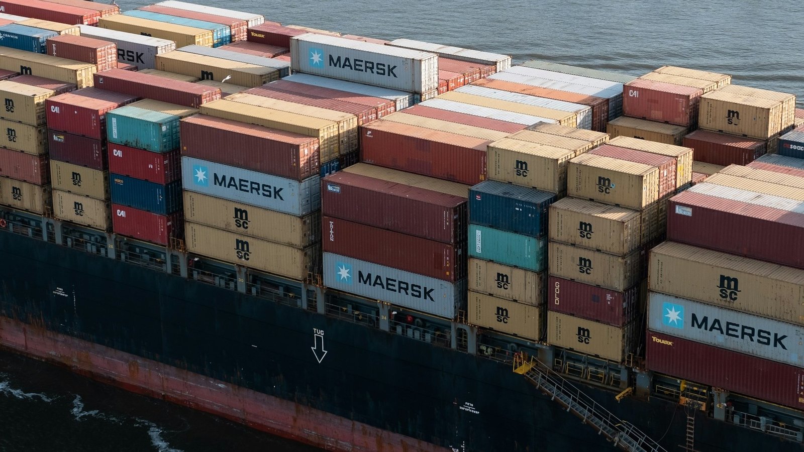 Auf dem Bild ist ein Ausschnitt eines Containerschiffes zu sehen, das mit bunten Containern beladen ist.