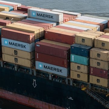 Auf dem Bild ist ein Ausschnitt eines Containerschiffes zu sehen, das mit bunten Containern beladen ist.