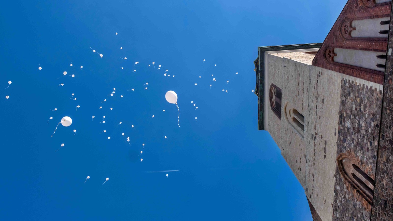 Weiße Luftballons die gegen einen blauen Himmel aufsteigen, rechts ein Kirchturm