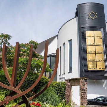 Das Foto zeigt die Synagoge Beith-Shalom der jüdischen Kultusgemeinde von Rheinland-Pfalz in Speyer. Im linken Bildvordergrund ist ein stilisierter Siebenarmiger Leuchter zu sehen. Im rechten Bildhintergrund das Gebäude der Synagoge.