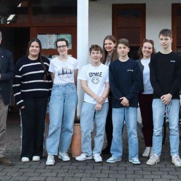 Zwei Männer mit grauen Haaren stehen links rechts neben ihnen stehen Jugendliche und eine junge Frau in einer Gruppe zusammen.