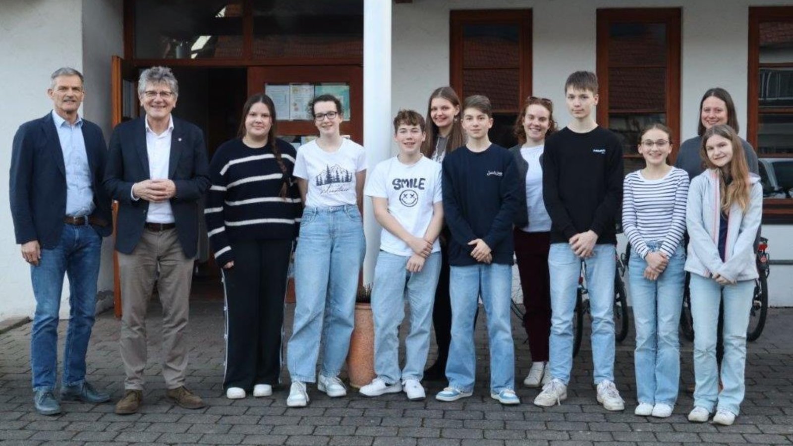 Zwei Männer mit grauen Haaren stehen links rechts neben ihnen stehen Jugendliche und eine junge Frau in einer Gruppe zusammen.