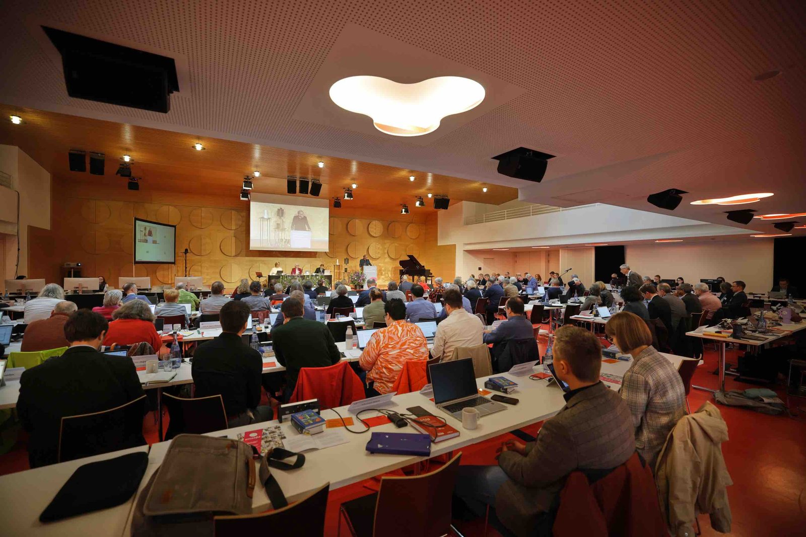 Im Stuttgarter Hospitalhof sitzen die Synodalabgeordneten mit Laptops an den Tischen. Vorne ist eine kleine Bühne mit einem Bildschirm und einem Rednerpult zu sehen.