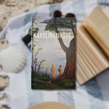 Buchtipp: „Karolinenhöhe“ im Vordergrund. Im Hintergrund ist eine Picknickdecke zu sehen, diese liegt auf Sand. Auf ihr liegt eine Sonnenbrille, eine Kamera, eine große Muschel sowie ein aufgeschlagenes Buch. 