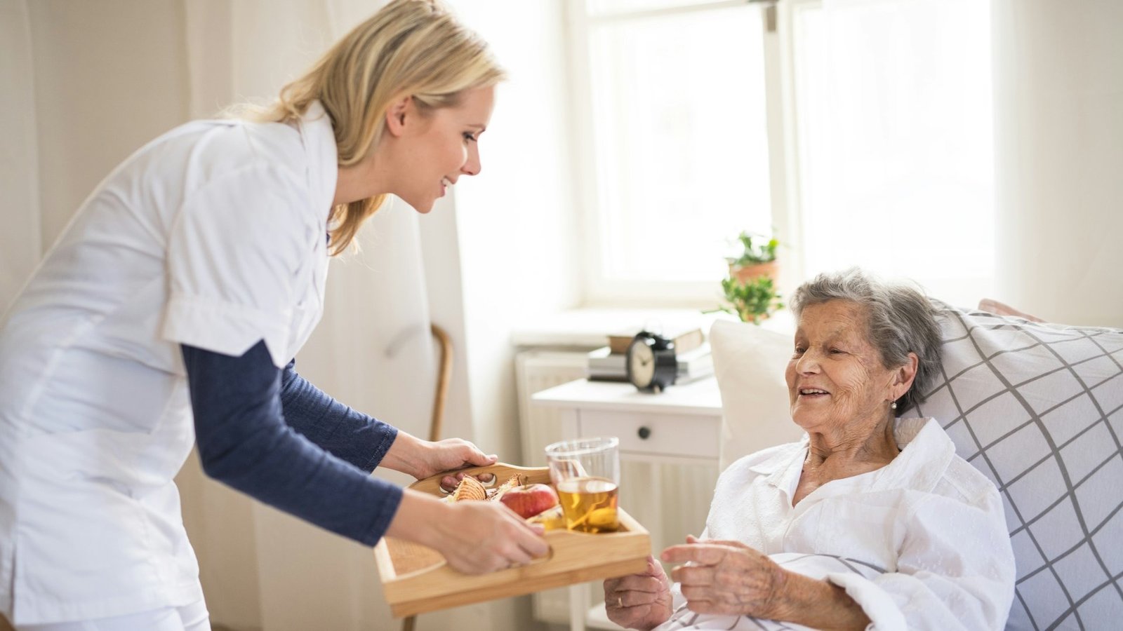 Pflegekraft bringt Seniorin Frühstück ans Bett.
