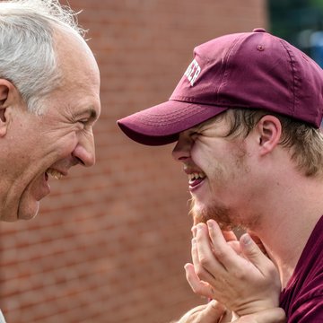 Ein älter Mann (links) und ein jüngerer Mann mit Mütze (rechts)lachen sich an.