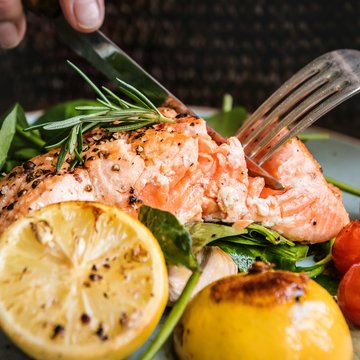Ein Teller mit einem gebratenen Lachsfilet, Zitronen und Tomaten