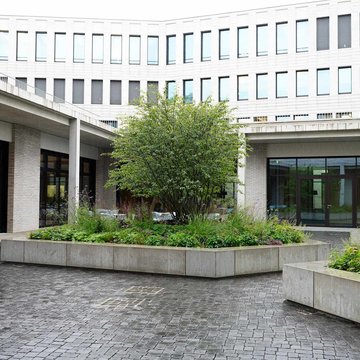 Zu sehen ist der Innenhof des neu gebauten Gebäudes des Oberkirchenrates in Stuttgart. Es ist ein helles Gebäude mit grün bepflanzten Inseln im Innenhof.