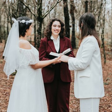 Ein Brautpaar – zwei Frauen – halten sich an den Händen. Zwischen ihnen steht eine Frau, die die beiden traut.
