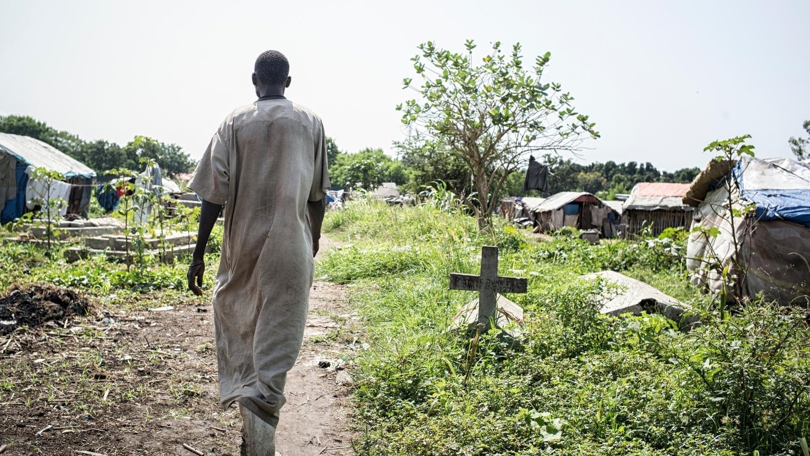 Eine Person, die von hinten zu sehen ist, läuft über einen Friedhof in Nordost-Afrika, auf dem mittlerweile Menschen wohnen. Rechts neben der Person ist ein Kreuz zu sehen.