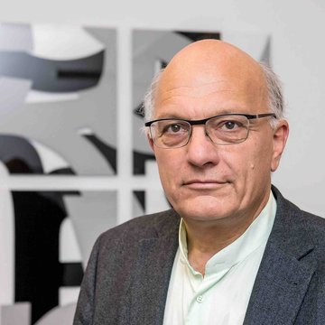 Das Foto zeigt Christian Staffa. Er trägt ein weißes Hemd und ein graues Jackett. Der ältere Mann hat eine Halbglatze und trägt eine Brille.