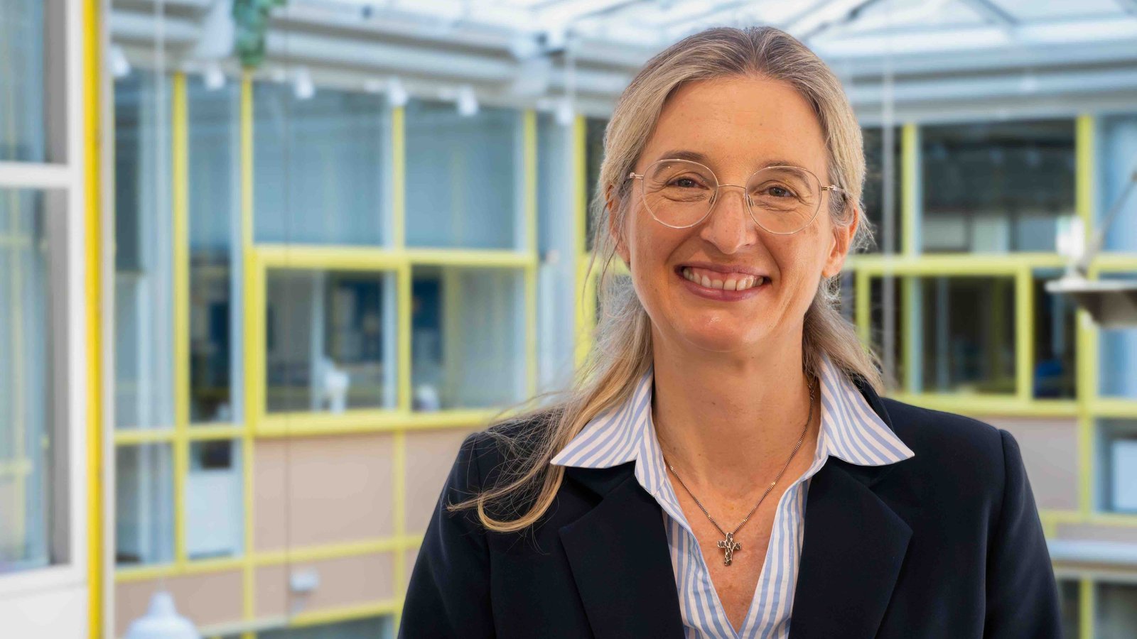 Das Foto zeigt Nina Lubomierski. Sie lächelt in die Kamera, trägt eine Bluse und einen schwarzen Blazer darüber. Sie hat lange blonde Haare und trägt eine Brille.