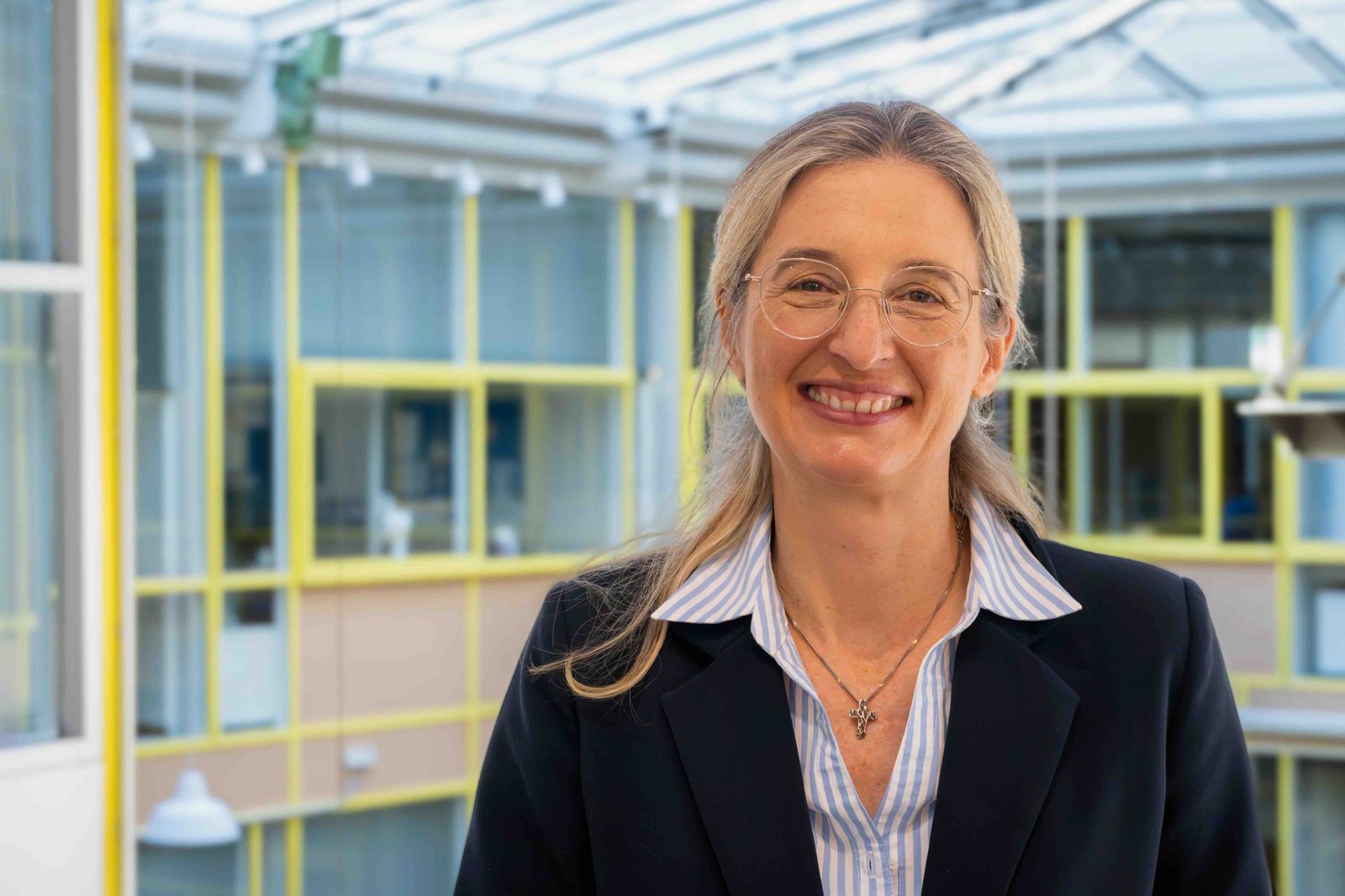 Das Foto zeigt Nina Lubomierski. Sie lächelt in die Kamera, trägt eine Bluse und einen schwarzen Blazer darüber. Sie hat lange blonde Haare und trägt eine Brille.