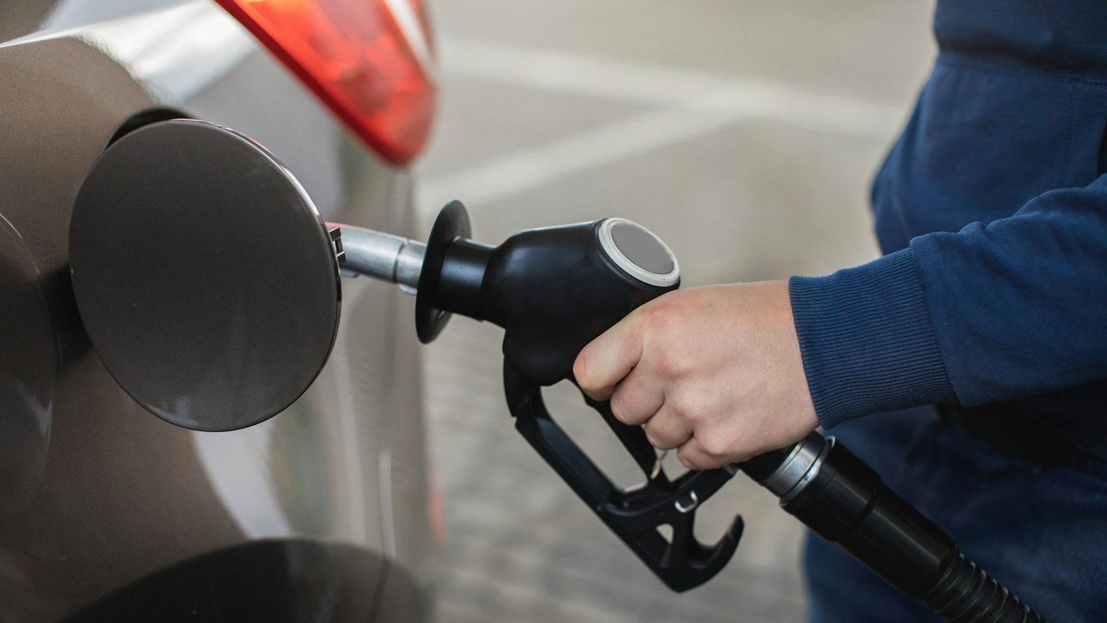 Eine Männerhand füllt an einer Tankstelle Benzin in den Tank eines Autos.