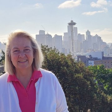 Carolyn Schott, eine Frau mit blonden schulterlangen Haaren steht vor der Skyline von Seattle.