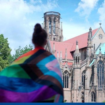 Eine junge Frau steht mit einer Regenbogenflagge vor der Stuttgarter Feuerkirche.