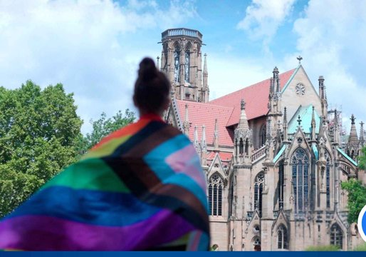 Eine junge Frau steht mit einer Regenbogenflagge vor der Stuttgarter Feuerkirche.