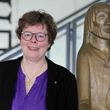Portraitfoto von Beate Hofmann. Die Frau hat Locken, trägt eine Brille, eine lilafarbene Bluse und einen schwarzen Blazer. Sie lächelt in die Kamera.