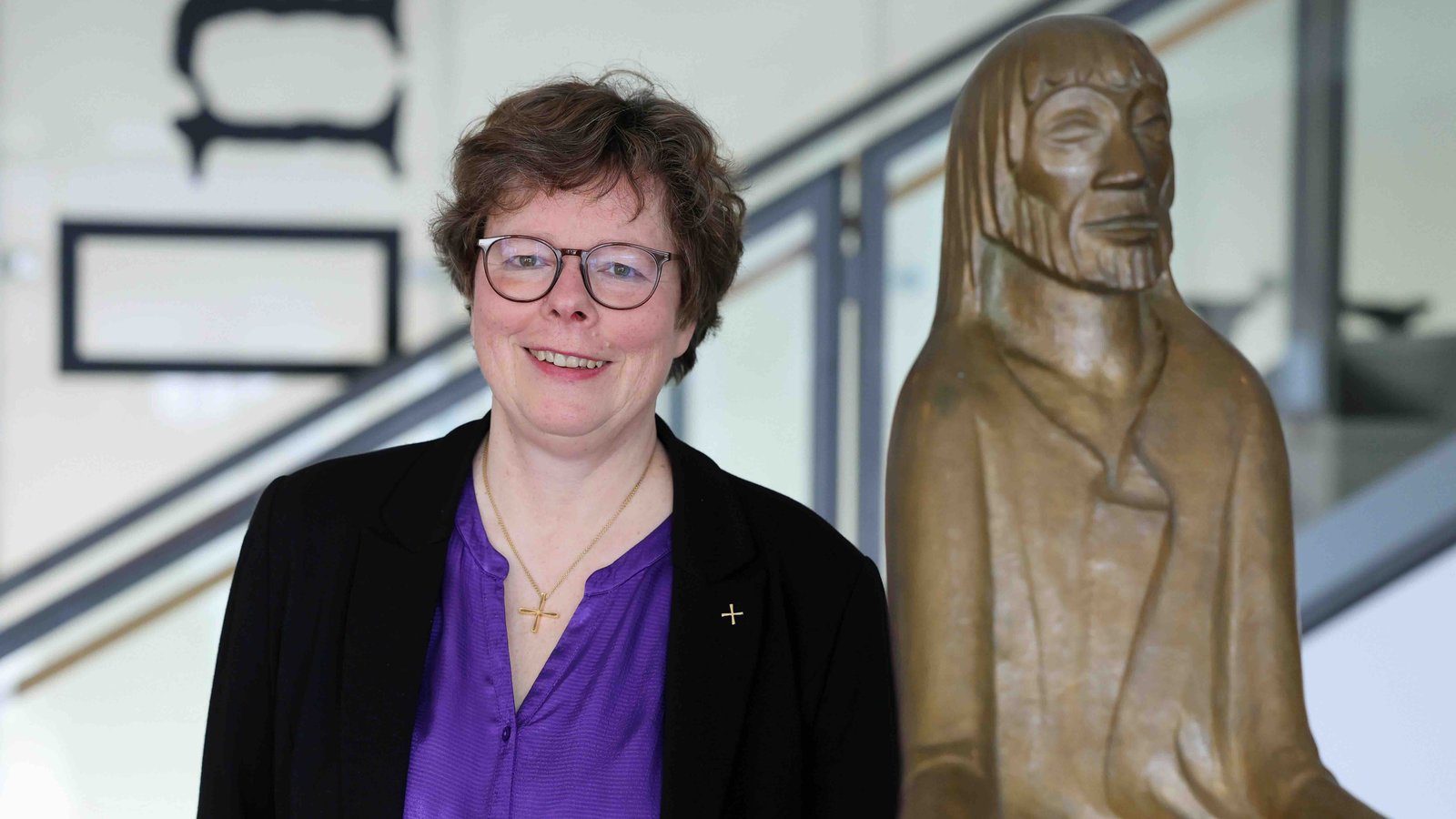 Portraitfoto von Beate Hofmann. Die Frau hat Locken, trägt eine Brille, eine lilafarbene Bluse und einen schwarzen Blazer. Sie lächelt in die Kamera.