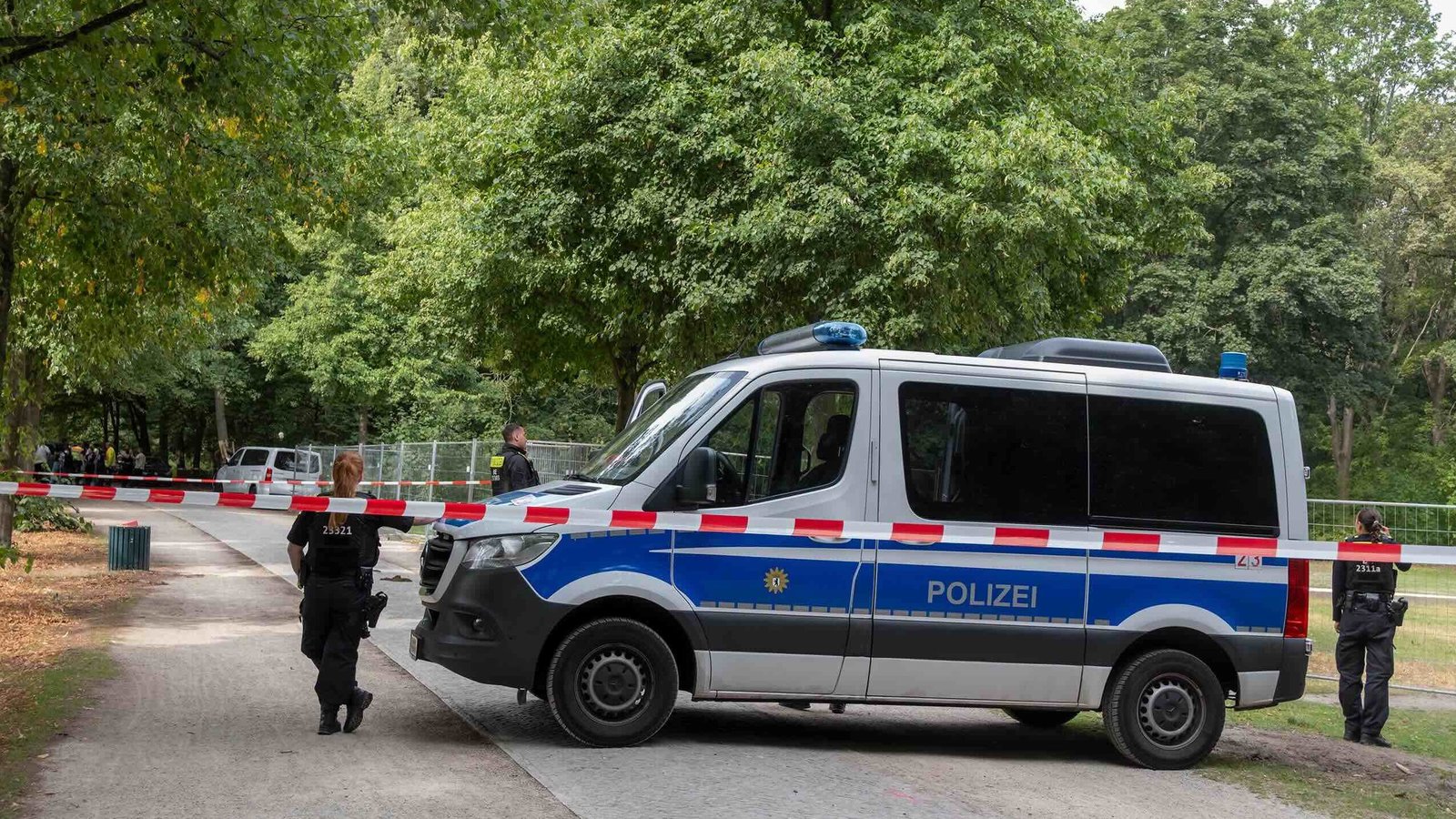 Beamte der Tatortforschung und Tatordokumentation der Polizei untersuchen den Tatort des gestrigen Anschlags auf den CSD im Berliner Tiergarten. Ein großes Polizeiauto steht hinter einer Absperrung mit rot-weißem Absperrband