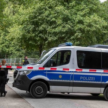 Beamte der Tatortforschung und Tatordokumentation der Polizei untersuchen den Tatort des gestrigen Anschlags auf den CSD im Berliner Tiergarten. Ein großes Polizeiauto steht hinter einer Absperrung mit rot-weißem Absperrband