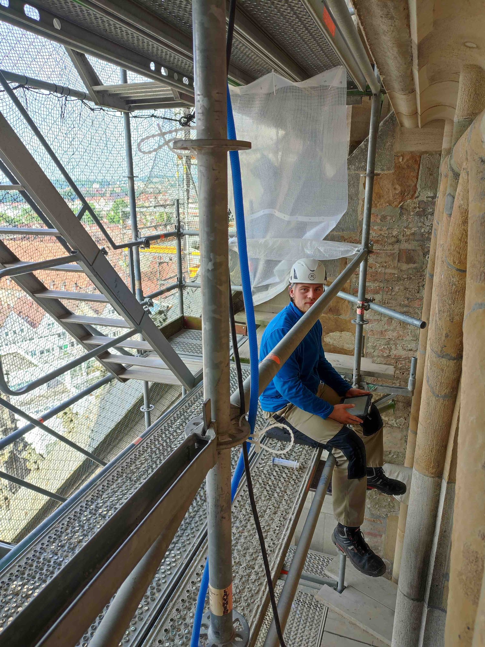 Junger Mann sitzt gesichert auf einem Gerüst auf dem Turm des Ulmer Münsters