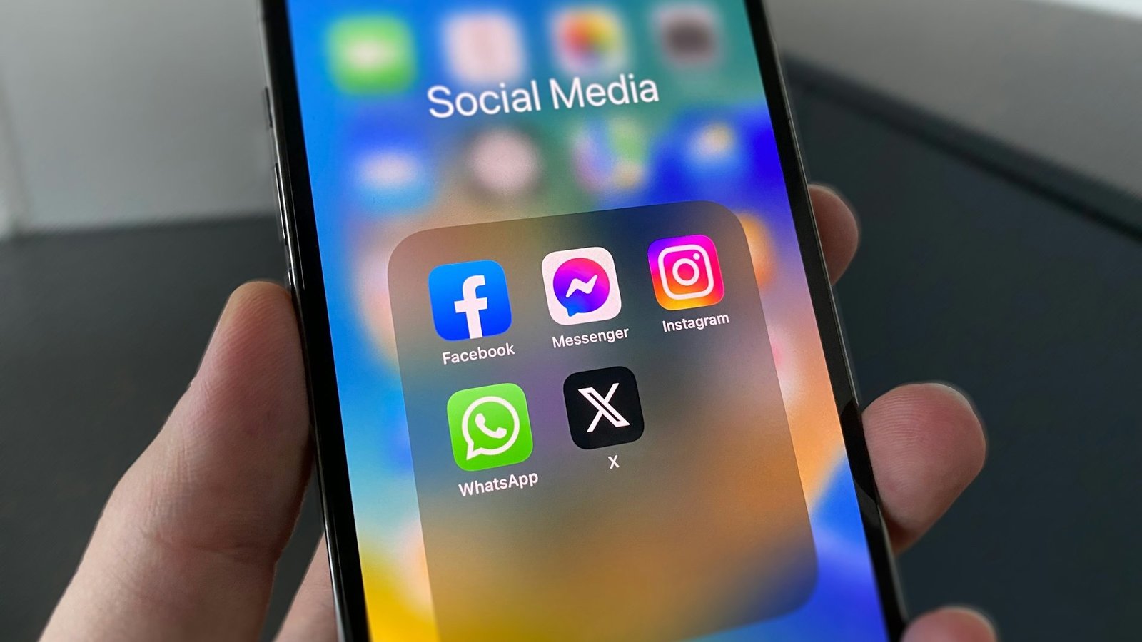 Ein Smartphone wird in einer Hand gehalten, der Bildschirm zeigt einen Ordner der mit "Social Media" überschrieben ist und die App-Symbolde von Facebook, Facebook Messanger, Instagram, WhatsApp und X (ehemals Twitter) zeigt.