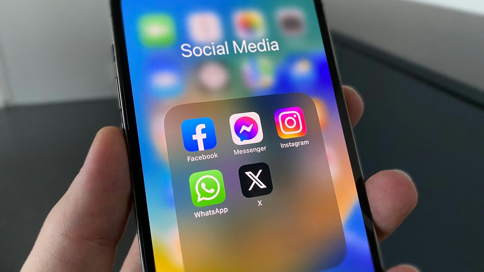Ein Smartphone wird in einer Hand gehalten, der Bildschirm zeigt einen Ordner der mit "Social Media" überschrieben ist und die App-Symbolde von Facebook, Facebook Messanger, Instagram, WhatsApp und X (ehemals Twitter) zeigt.