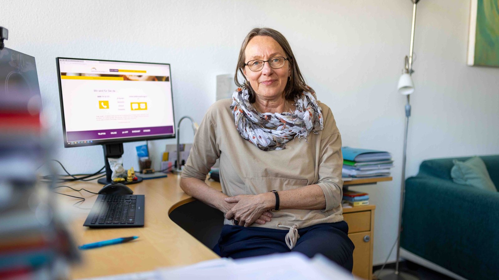 Eine Frau (Martina Rudolph-Zeller) sitzt an einem Schreibtisch. Im Hintergrund sind zwei Bildschirme zu sehen.