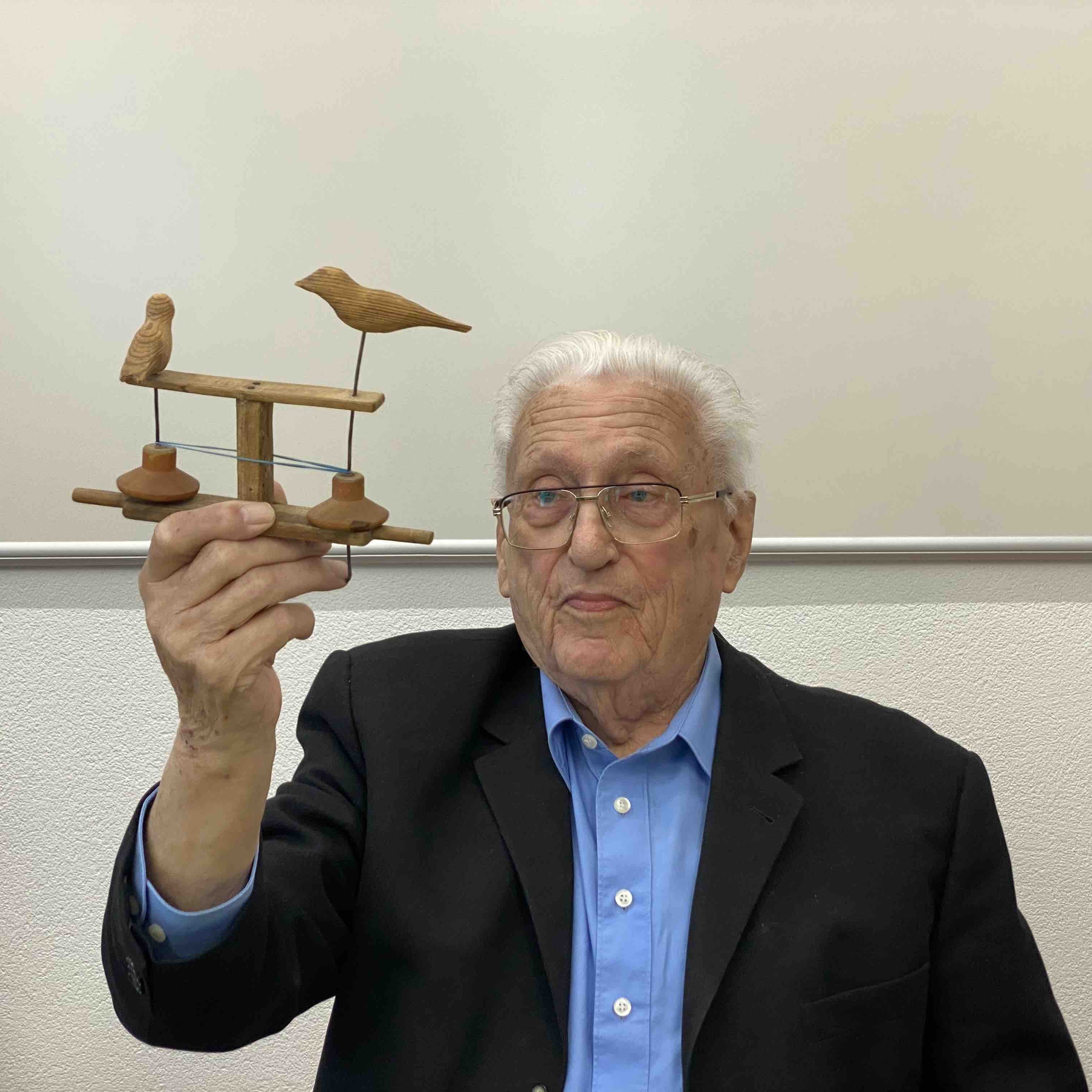 Franz-Karl Weiß hält ein Holzspielzeug in Form von Vögeln in der Hand