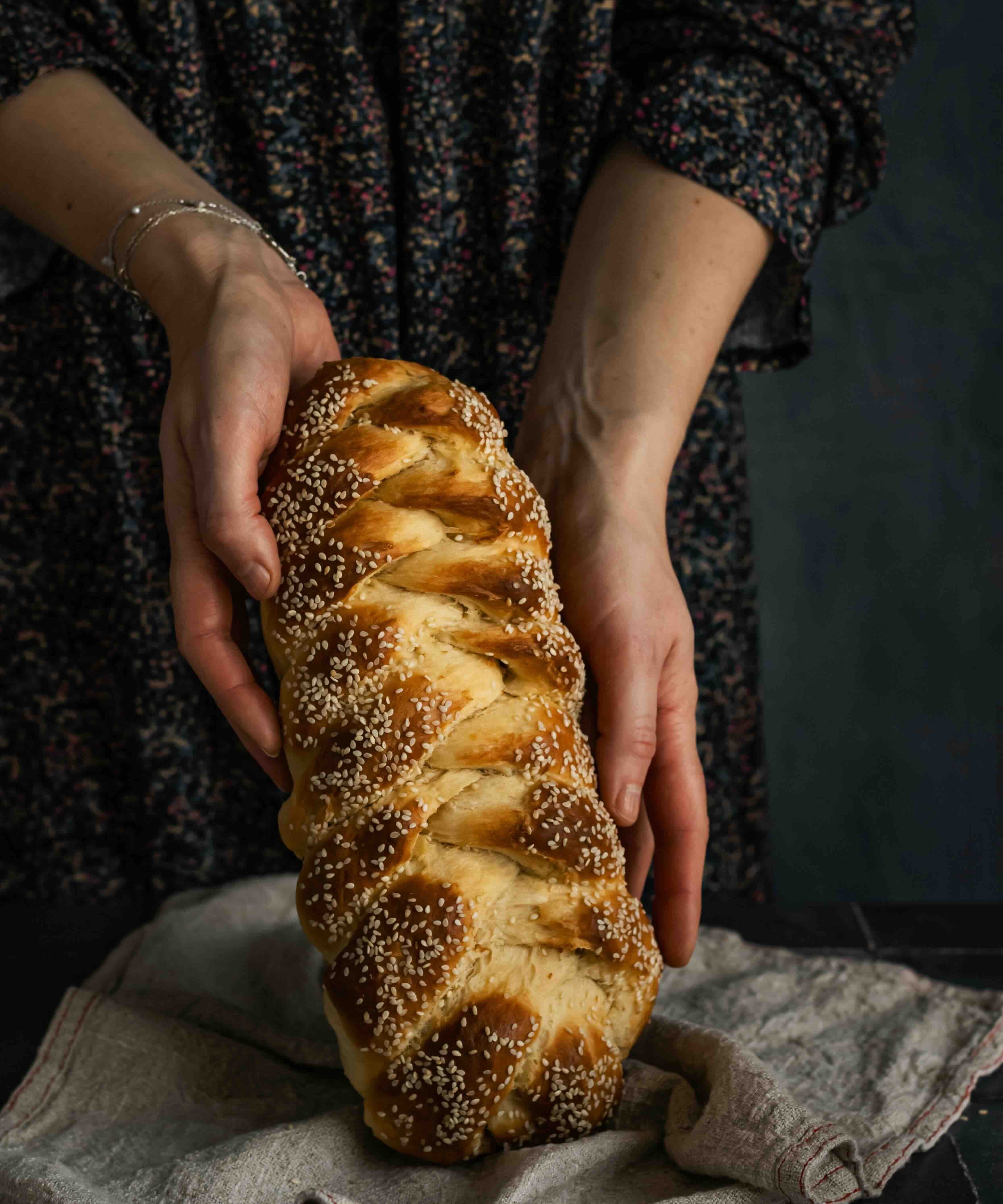 Die Aufnahme zeigt eine Frau, die ein frisch gebackenes Brot, Challa, in den Händen hält.